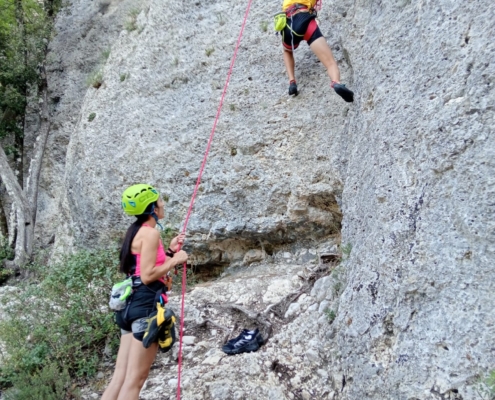 Bambino che scala una falesia in Umbria con casco e imbrago, seguito da un istruttore